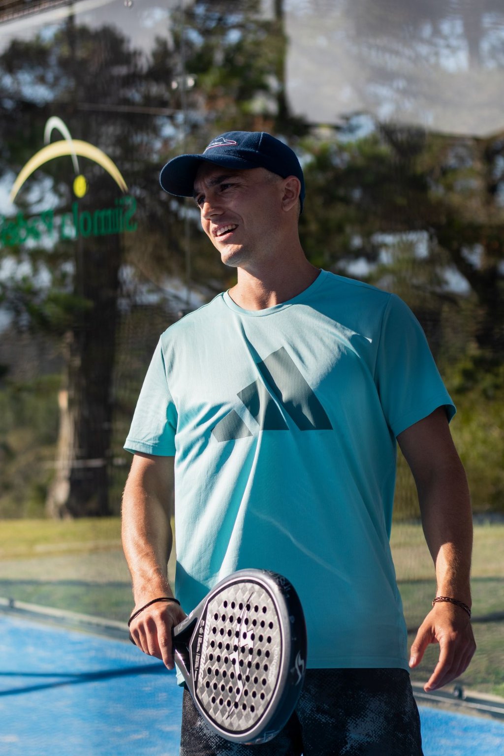 Smiling padel player holding a racket on a sunlit outdoor court