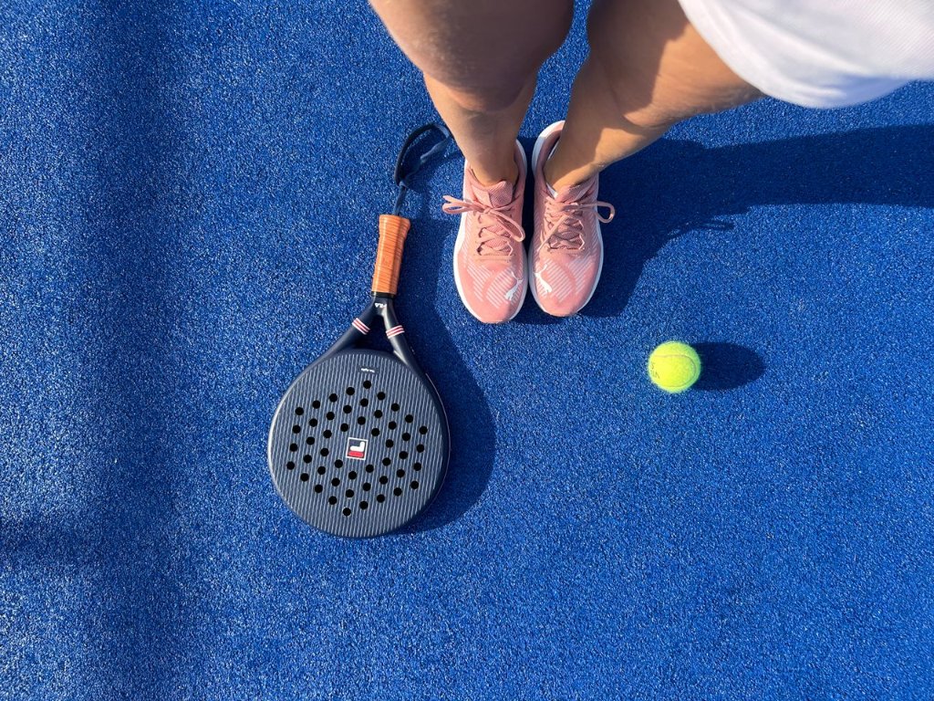 Overhead view of court shoes, a padel racket and a ball