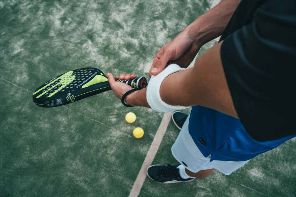 Padel player adjusting a wristband on court with racket and balls