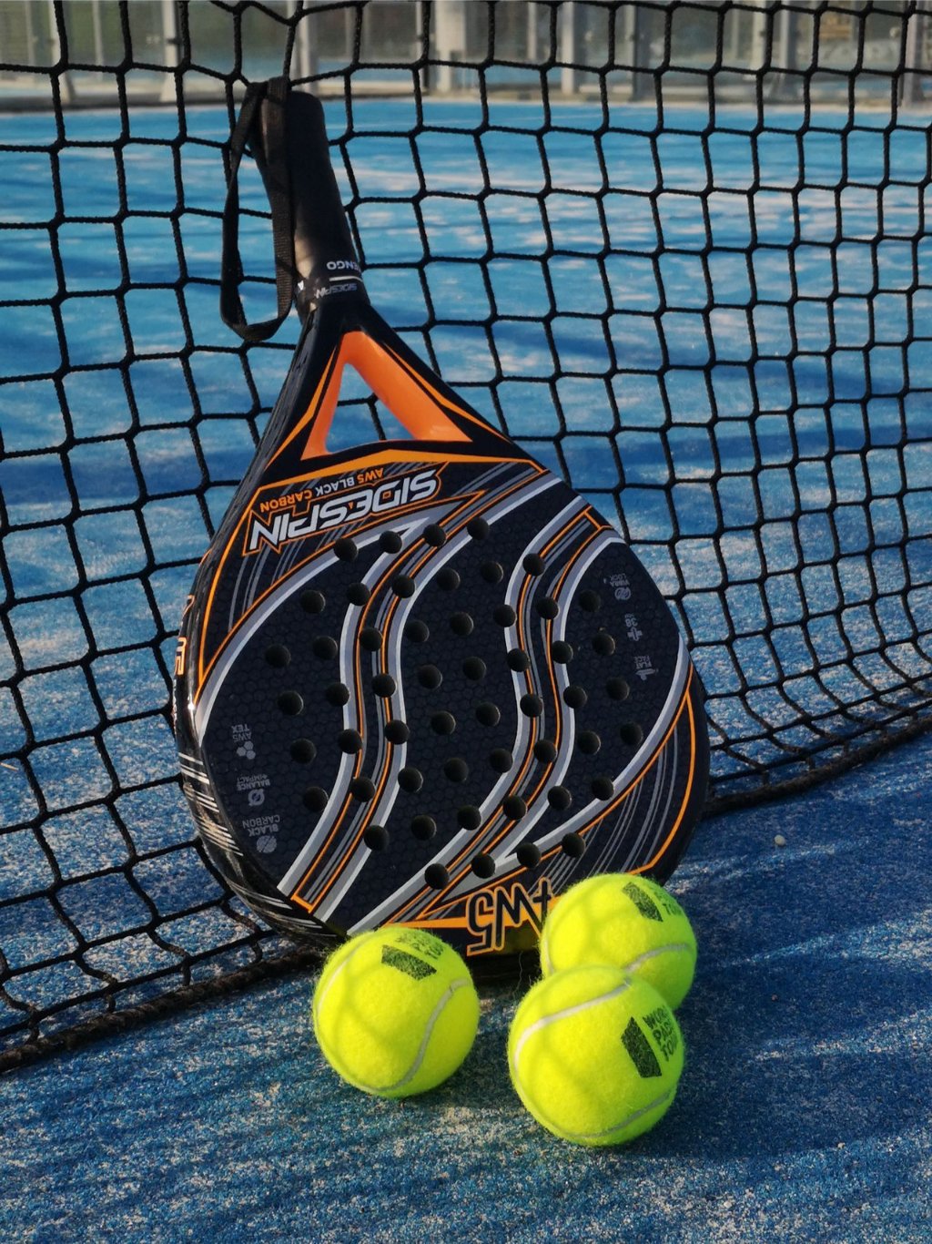 A padel racket and three balls beside the net
