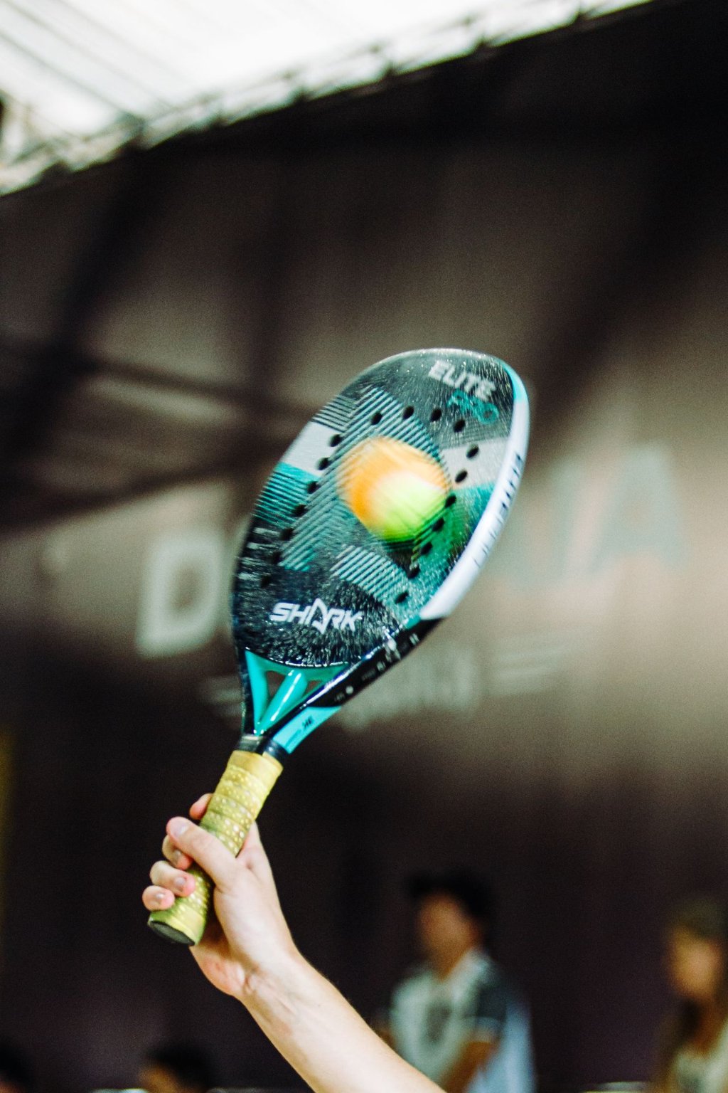 A padel racket striking a ball indoors