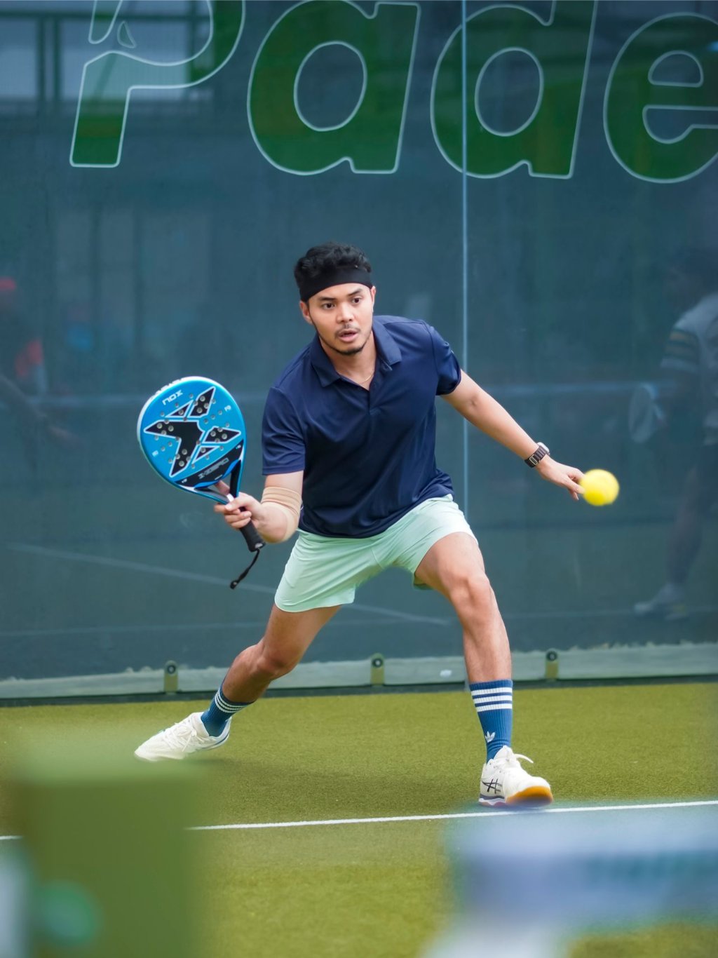 Padel player lunging for a forehand on an outdoor glass court